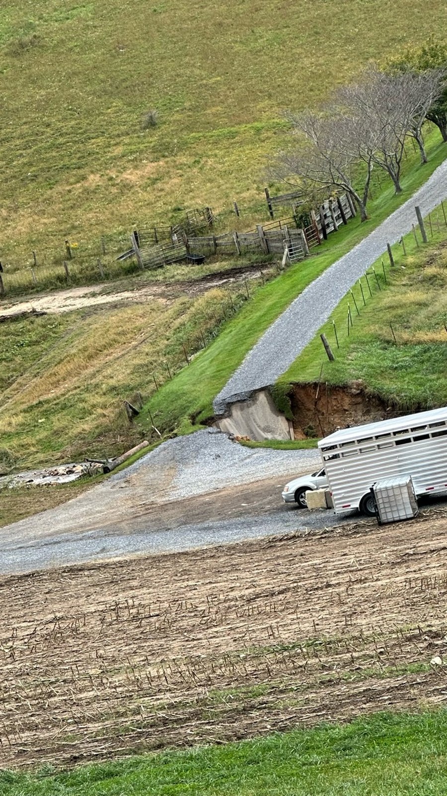 A gravel farm driveway broken by a deep washout where floodwater tore out the culvert.